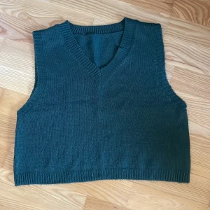 Grön stickad väst - Säljer en snygg grön stickad väst med v-ringning. Perfekt för lager-på-lager-stil och passar bra över en långärmad tröja. Västen har en ribbad kant vid ärmhålen och nederkanten.