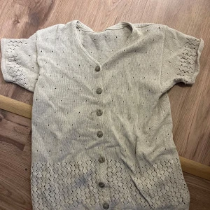 Beige kortärmad kofta med knappar - Säljer en jättesöt beige kofta med korta ärmar och knappar framtill. Den har ett fint hålmönster som ger en luftig känsla. Perfekt för vår och sommar!