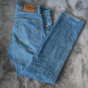 Blå jeans från Levi's - Säljer ett par klassiska blå jeans från Levi's. De har en normal passform och är tillverkade i slitstarkt denim. Perfekta för en avslappnad stil. Jeansens design inkluderar den ikoniska läderpatchen och den röda Levi's-loggan på bakfickan. De sitter väldigt bekvämt intil kroppen, jag som har dem nu är 188 cm. Tveka inte att fråga för mer information. 