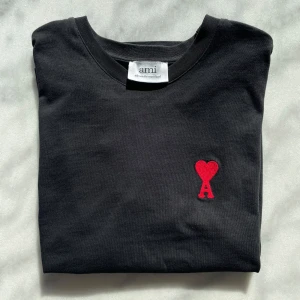 Svart t-shirt från Ami - Snygg svart t-shirt från Ami med ett rött broderat hjärta och bokstaven A på bröstet. Perfekt för en stilren look.