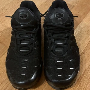 Svarta Nike sneakers - Snygga svarta Nike sneakers med TN-logo på hälen. Skorna har en stilren design med snörning och en robust sula. Perfekta för en sportig look. Bra skick, använts några få gånger. 