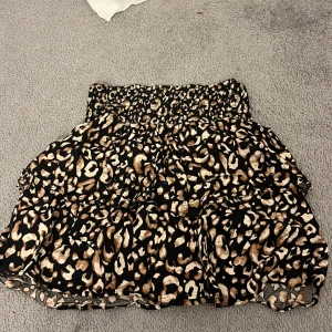 Leopardmönstrad kjol från Pigalle - Snygg leopardmönstrad kortkjol från Pigalle i storlek XS. Kjolen har en elastisk midja och volanger som ger en fin rörelse. Perfekt för att lägga till lite djurmönster i garderoben!