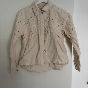 Beige skjorta med broderade detaljer - Superfin beige skjorta från KIDS ONLY i bomull med broderade spetsdetaljer över axlar och bröst. Skjortan har knappar framtill, råa kanter nertill och långa ärmar. Perfekt för dig som gillar en söt och avslappnad stil. Pris kan diskuteras💗