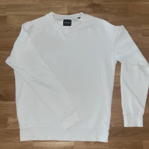 Vit sweatshirt från Jack & Jones - Vit sweatshirt från Jack & Jones i klassisk stil med rund hals och ribbade muddar vid ärmslut och nederkant. Tröjan är långärmad och har en clean look utan mönster eller tryck. Materialet är mjuk bomull som känns skön mot huden. Storlek M. Använd Max 5 gånger. Säjes för lågt pris på grund av en liten fläck på tröjan. Pris kan förhandlas.