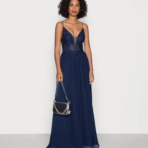 Marinblå långklänning med spets och pärlor - Elegant marinblå långklänning med smala axelband och djup v-ringning. Livet är dekorerat med spets och pärlor, vilket ger en lyxig känsla. Kjolen är i ett lätt, flytande material som faller snyggt. Perfekt för bal eller fest. Den är liten i storleken så skulle säga att den är mer som 38/40