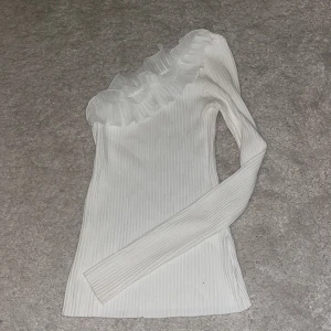 Vit ribbad oneshoulder topp med volang - Supersnygg vit ribbad topp med oneshoulder-design och lång ärm. Toppen har en bred volang i mesh längs halsringningen. Inga defekter 💞