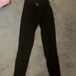 Svarta ridbyxor med hög midja - Svarta ridbyxor med hög midja och tight passform. Byxorna har förstärkningar på insidan av benen och klassisk knapp framtill. Perfekta för dig som gillar ridning och vill ha en stilren look i stallet☺️