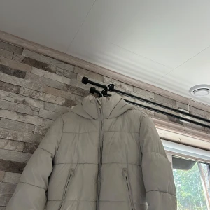 Beige pufferjacka från Zara med huva - Säljer en beige pufferjacka från Zara i storlek S. Jackan har en stor huva, två dragkedjeförsedda fickor och quiltad design. Perfekt för kalla dagar och riktigt snygg till streetwear-looken. Jackan är tillverkad i syntetmaterial och stängs med dragkedja framtill.