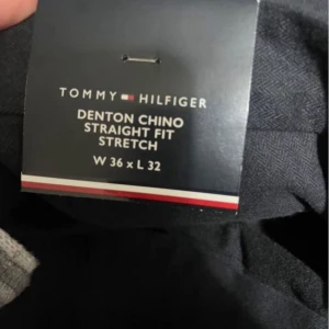 Svarta Denton Chinos Tommy Hilfiger - Säljer ett par svarta Denton Chino byxor från Tommy Hilfiger i straight fit med stretch. Klassisk rak passform och stilren look, perfekta till sneakers eller boots. Materialet är mjukt och följsamt för extra komfort.