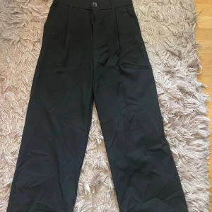 Svarta vida kostymbyxor - Snygga svarta kostymbyxor med hög midja och vida ben. Klassisk look med knapp och dragkedja framtill, perfekta för en clean och stilren outfit. Passar dig som gillar en loose fit och vill ha en modern siluett. Kostymbyxorna är från Zara