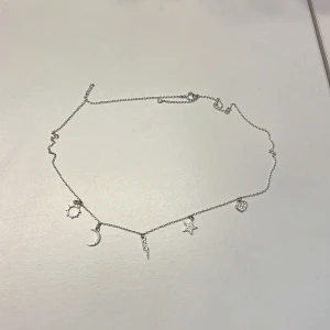 Silverhalsband med berlocker - Snyggt silverfärgat halsband med tunna kedja och fem berlocker: sol, måne, blixt, stjärna och hjärta. Perfekt för dig som gillar detaljer och vill ha något unikt runt halsen. Berlockerna har glittriga stenar som ger extra shine.