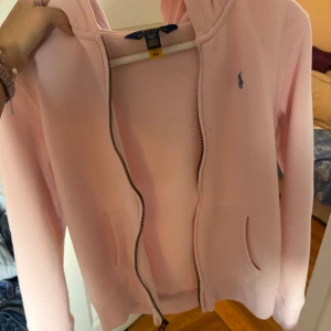 Rosa hoodie från Polo Ralph Lauren - Säljer en ljusrosa hoodie från Polo Ralph Lauren i storlek XL (16 år), sitter som XS/S. Tröjan har huva, dragkedja framtill och två fickor. Använd 2 - 3 gånger och är i bra skick. Skriv privat för fler bilder.