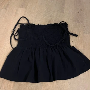 Svart smockad linnetopp från SHEIN - Supersöt svart linnetopp från SHEIN med smockad överdel och volangig nederkant. Toppen har tunna knytband som axelband och en luftig, flowy känsla. 