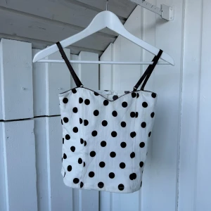 Prickig linnetopp från Zara - Supersöt vit linnetopp från Zara med svarta prickar och tunna svarta axelband. Toppen har en lätt figurnära passform och är perfekt för dig som gillar retrovibbar och lekfull stil. Materialet är mjukt och lätt, perfekt för varma dagar.