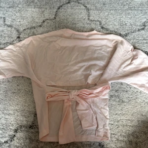 Ljusrosa omlottopp från Nelly XS - Supersöt ljusrosa omlottopp från Nelly i mjuk bomull. Toppen har korta ärmar, rund halsringning och en snygg knytning i ryggen som ger en extra detalj. Perfekt för dig som gillar en feminin och enkel stil.