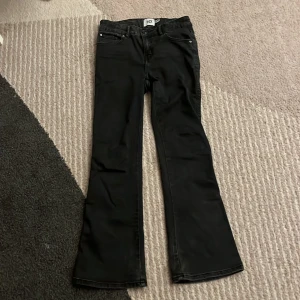 Svarta bootcut jeans från 157, stl 150 - Svarta jeans från 157 i modellen 90's Boot Star. Byxorna har klassisk femficksdesign, snygg bootcut-passform och är tillverkade i ett stretchigt jeanstyg. Perfekta för dig som gillar retrovibbar och vill ha en bekväm men trendig look.