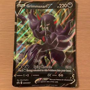 Grimmsnarl V - Cool och glittrig Pokémonkort med Grimmsnarl V! Perfekt för dig som samlar eller spelar Pokémon TCG. Kortet har en unik design och kraftfulla attacker. Observera att det finns en tydlig repa i mitten av kortet.