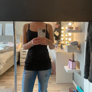 Svart linnetopp med smala axelband - Enkel och stilren svart linnetopp med smala axelband och rundad halsringning. Sitter tight mot kroppen och är perfekt att matcha med jeans eller kjol. 