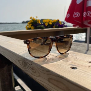 Ray-Ban Boyfriend - Säljer ett par Ray-Ban Boyfriendmed brunmelerad båge och rektangulär form. Glasen är tonade i brunt och bågen har ett snyggt sköldpaddsmönster. Tillverkade i Italien, storlek 60-15. Perfekt för dig som vill ha klassisk stil med en modern twist.