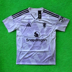 Manchester United bortatröja Adidas - Snygg Manchester United bortatröja från Adidas med lila och vita toner, svart klubbmärke och sponsorlogga. Tröjan har klassiska Adidas-ränder på axlarna och är tillverkad i lätt, ventilerande polyester med AEROREADY-teknologi. Perfekt för dig som vill sticka ut på planen.