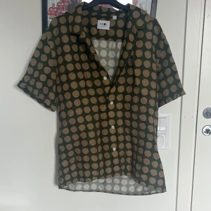 Grön prickig skjorta från NN07 - Säljer en grön skjorta från NN07 med beige prickar. Skjortan har korta ärmar, klassisk krage och knäppning framtill. Stl L o modellen är regular fit 