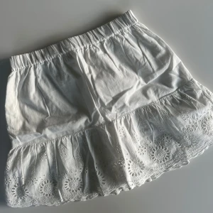 Vit volangkjol från Kappahl - Supersöt vit kortkjol från Kappahl med broderade blommor och volangkant. Kjolen har resår i midjan för en skön passform. Perfekt för sommarens alla äventyr!💗