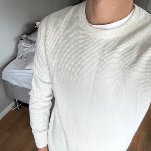 Vit stickad tröja med struktur - Säljer en stilren vit stickad tröja med diskret strukturmönster. Tröjan har rund halsringning och långa ärmar, perfekt för dig som gillar en clean och enkel look. Passformen är normal och materialet känns mjukt mot huden.