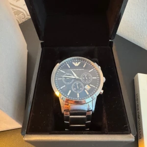 Emporio Armani silverfärgad klocka - Stilren klocka från Emporio Armani med mörkblå urtavla, silverfärgat armband i metall och flera små urtavlor för extra funktioner. Klassisk rund form och tydliga indexmarkeringar. Perfekt accessoar för dig som gillar en clean och modern look.