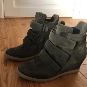 SÖKER !!!!!!!!!Mörkgröna kilklack sneakers i mocka - Snygga mörkgröna sneakers med kilklack och breda kardborreband. Skorna är gjorda i mocka och har en platt sula framtill. Perfekta för dig som vill ha lite extra höjd men ändå en sportig look.