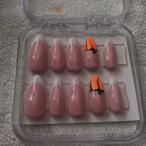 Press ons pumpkin French  - Säljer ett set med press-on naglar i mandelform. Naglarna är ljusrosa med vit fransk tipp och två naglar har en cool orange och svart nail art. Kommer i en genomskinlig ask, perfekta för att snabbt fixa snygga naglar hemma.