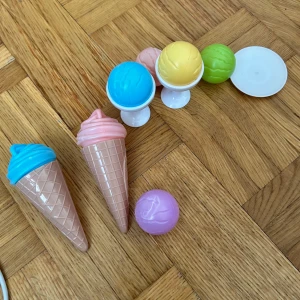 Färgglada glassar  - Bilderna visar färgglada leksaksglassar i plast, perfekta för låtsaslek och att skapa egna glasskreationer. Innehåller strutar, glasskulor i olika färger och glasskålar. Passar för barn och unga som gillar att leka café eller glasskiosk. Ingen bok syns på bilderna.