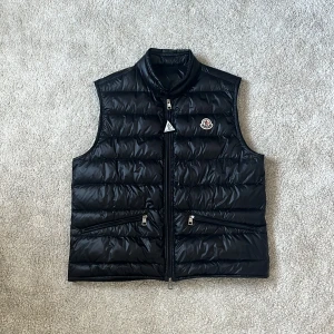  Moncler Gui väst - Hej! Säljer denna extremt snygga Moncler Gui väst!  Väldigt fint skick! Som ny förutom att det är 3 osynliga pinholes. 2019 modell! Otroligt fet och ett måste att ha i sin garderob! Perfekt att ha över en T-shirt eller under en jacka! Storlek 2 vilket motsvarar S-M! En Moncler triangel fås med som en rolig accessoar till västen 😁västen är en favorit men behöver en storlek upp (3) egentligen därför säljer jag den😅. Endast 1 användare sedan innan som knappt använt den. Skriv vid minsta intresse!🔹
