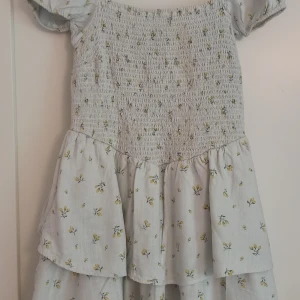 Ljusblommig kort klänning från H&M - Supersöt klänning från H&M med mockad överdel och volangkjol💕 Storlek L. 17% lin. (Finns en avlång fläck på överdelen, vilket syns på högra sidan! Inte provat behandla) 