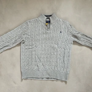 Grå stickad tröja Polo Ralph Lauren - Snygg grå stickad tröja från Polo Ralph Lauren med klassiskt kabelmönster och half zip vid halsen. Tröjan har långärmade ribbade muddar och liten broderad logga på bröstet. Perfekt för dig som gillar stilren och tidlös design. Köpt för 1500kr mitt pris 799kr! Mycket bra skick användning syns ej. Pris går att diskutera vid snabb affär