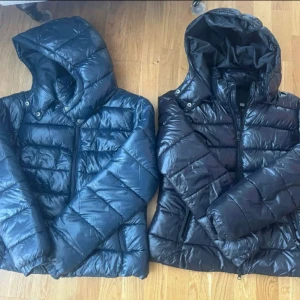 Lager 157 pufferjacka - Två pufferjackor med huva i svart och mörkblått. Dom är helt nya, aldrig använts. Båda har quiltad design, dragkedja framtill och långa ärmar. Perfekta för kyliga dagar och även nu perfekt inför hösten. Det ger en sportig vibe. Snygga att bära till jeans eller mjukisbyxor. Dom är köpta ifrån lager 157. Om du är intresserad om priserna så säljs båda tillsammans för 500kr, men varsin så säljs dom för 250. Priset kan diskuteras.