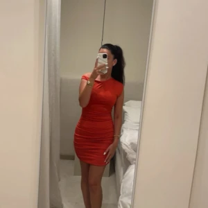 Röd kortklänning från SHEIN - Snygg röd kortklänning från SHEIN i storlek S. Klänningen har en figurnära passform med rynkade detaljer längs sidorna och korta ärmar. Materialet är mjukt och stretchigt, perfekt för att framhäva siluetten. Enkel och stilren design som ger en trendig look.