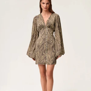 Adoore klänning - Säljer en kort klänning med zebramönster i beige och bruna toner. Klänningen har djup v-ringning, långa puffärmar och knappar hela vägen framtill. Materialet känns lätt och luftigt. Endast använd två gånger och extraknappar kommer med, nypris 1495kr. Ganska liten i storlek så passar även 36💗