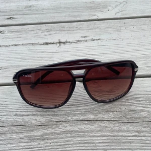  Vestimo - Snygga pilotformade solglasögon från Vestimo med mörkröda glas och svart plastbåge. Glasen har en cool toning och bågen har en metallisk detalj vid sidorna. Perfekt för dig som vill sticka ut med en retro vibe.