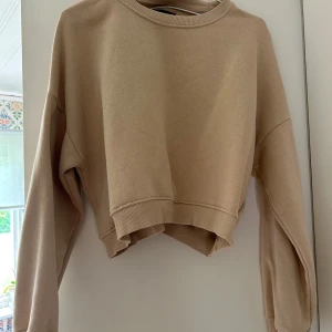 Beige croppad sweatshirt från 157 - Säljer en beige croppad sweatshirt från 157 med rund hals och långa ärmar. Tröjan har ribbade muddar vid hals och ärmslut samt en loose passform. Perfekt för chill dagar och enkel att matcha med jeans eller leggings.