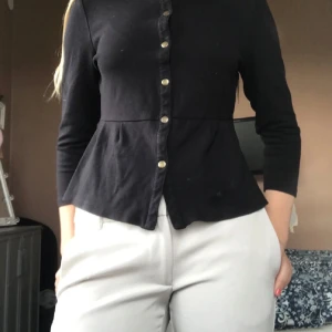 Svart kofta med knappar från Newhouse - Stilren svart kofta från Newhouse med rund halsringning och snygga metallknappar på framsidan. Den har korta armar vilket ger en klassisk look. Den sitter ganska tajt på kroppen. Enkel och klassisk design som funkar till det mesta. Pris kan diskuteras💓