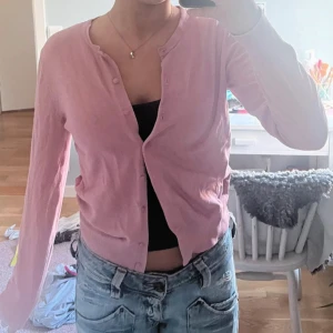 Ljusrosa kofta med knappar - Söt ljusrosa kofta med rund halsringning och knäppning framtill. Långärmad och i ett tunt, mjukt material som känns skönt mot huden. Perfekt att slänga över ett linne eller t-shirt för en chill look.