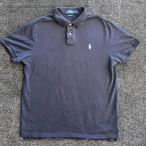 Ralph Lauren pike - Snygg mörkblå pikétröja från Polo Ralph Lauren med klassisk krage och två knappar framtill. Tröjan har korta ärmar och det ikoniska broderade logot på bröstet. Materialet är mjuk bomull som känns skönt mot huden. Perfekt för en chill och stilren look. Storlek L, skick 9/10, pris går att diskutera✅