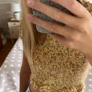Blommig topp  - Supersöt magtröja från Lindex med blommigt mönster i gult, rosa och grönt. Toppen har korta puffärmar, smockad kropp och volangkant vid ärmslut och nederkant. Säljer för att den inte kommer till användning, inte använd mycket och inga defekter. Står att det är stl 146 men passar mig som har XS-S. Kan köpas med koftan som jag har på mig i bild två. Bara toppen för 50 kr och med koftan 80 kr, man kan också bara köpa koftan för 50 kr, annons finns i min profil. Hör av er om ni är intresserade!❤️