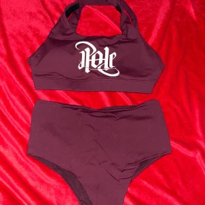 Vinrött Poledance set med hög midja - Vinrött set från IamPole med sportig topp och högmidjad underdel. Toppen har breda axelband som korsas i ryggen och vit logga framtill. Underdelen har matchande logga bak. Snygg och bekväm modell i stretchigt material, perfekt både för nybörjare och proffs