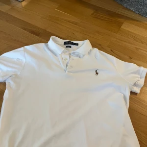 Vit piké från Polo Ralph Lauren - Klassisk vit pikétröja från Polo Ralph Lauren med broderad logga på bröstet. Slim fit-modell med korta ärmar och krage med knappar. Perfekt för en stilren och sportig look.