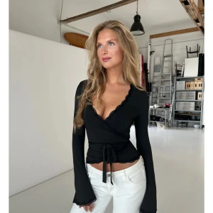 Svart knyttopp  - Säljer en svart omlottopp med långa ärmar, knyt i midjan och spetsdetalj vid urringningen. Helt oanvänd med lappen kvar!