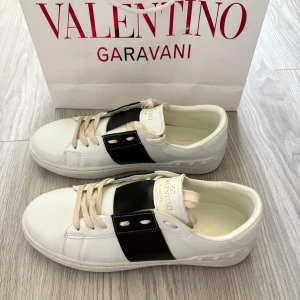 Valentino Garavani Open med svart detalj stl 42/43 - Säljer ett par vita Valentino Garavani Open sneakers med svart band över mitten. Skorna har rund tå, platt sula och ikoniska nitar baktill. Köpte dom på plick förra veckan men var för små för min son. Enl den annonsen stl 43, men skulle tro det är 42. Innermåttet 27 cm, se bild. 