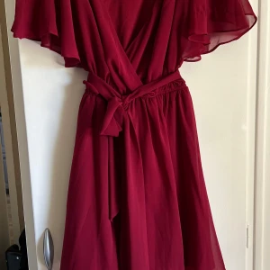 Vinröd sommarklänning  - Säljer en vinröd somrig klänning från Goddiva London med v-ringning, volangärmar och knyt i midjan. Klänningen är tillverkad i 100% polyester och har en luftig, elegant känsla. Perfekt för sommarens tillfällen! Använd en gång, inga skavanker. Storlek 36 men passar 34-38
