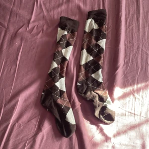 Bruna och beige knästrumpor med argylemönster - Säljer ett par brun-beige ridstrumpor från märket CRW. Strumporna är perfekta för en ridlektioner, uteritter eller stall häng! Materialet är mjuk och väldigt stretchigt. Säljer dessa pågrund av att jag har slutat på ridning och kommer inte till användning! Strumporna är i storlek 35-39! Skriv för fler frågor eller intresse!💕