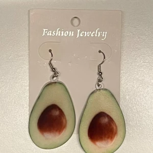 Avokado örhängen - Roliga örhängen formade som avokadohalvor med kärna. Perfekt för dig som vill sticka ut med ett unikt och färgglatt smycke. Hängande örhängen med krok i metall.